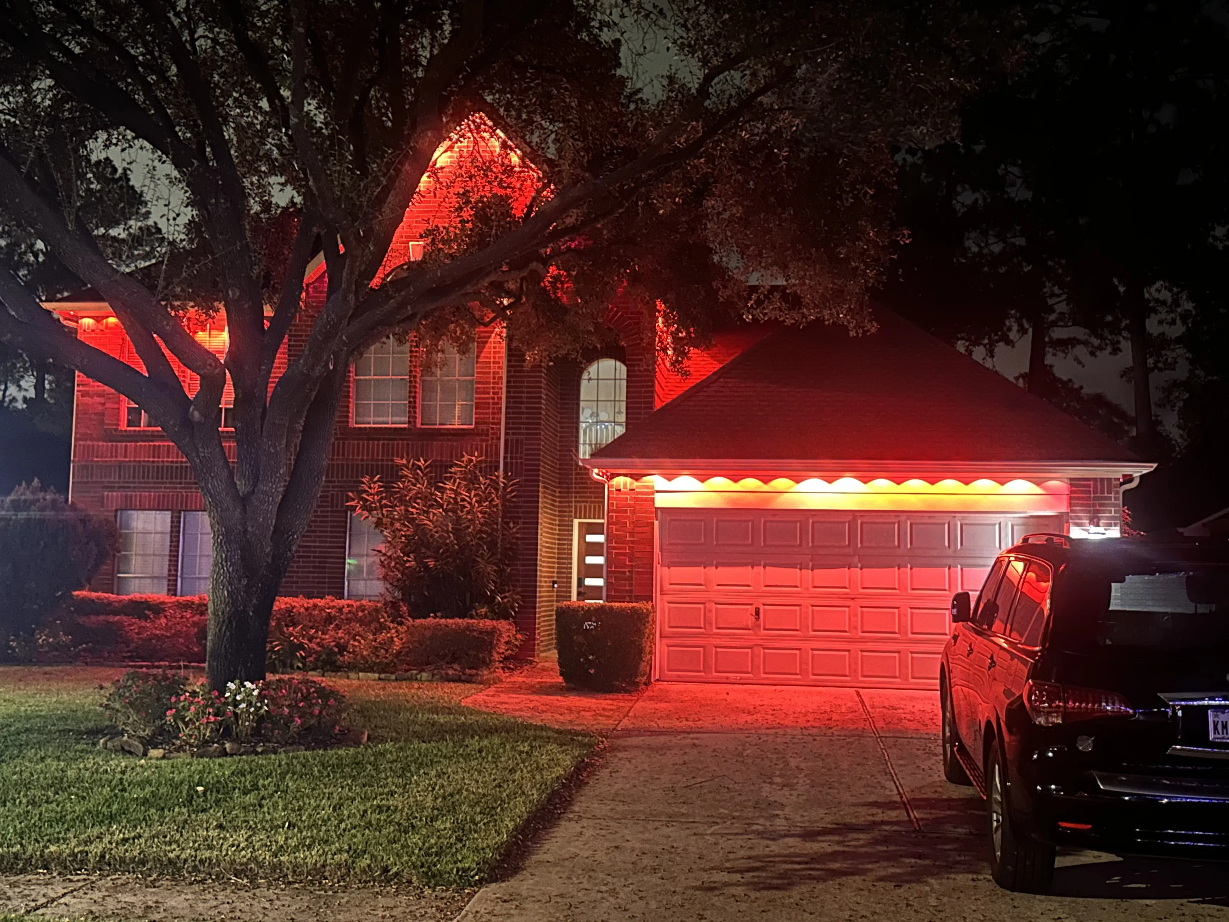 Red accent lighting on brick home exterior, garage, and tree at night