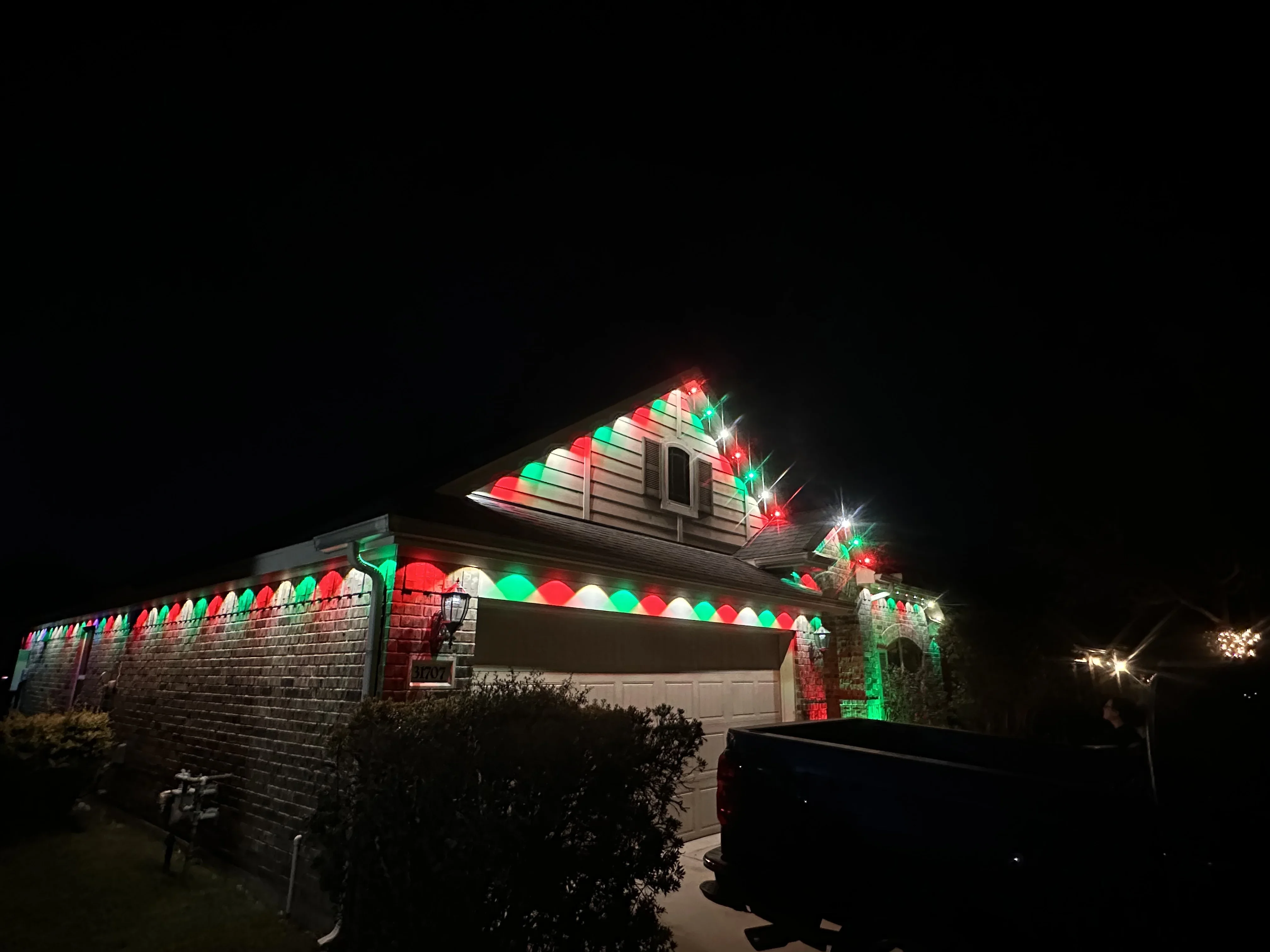 Brick home at night with red, green, and white holiday lights on roofline and garage