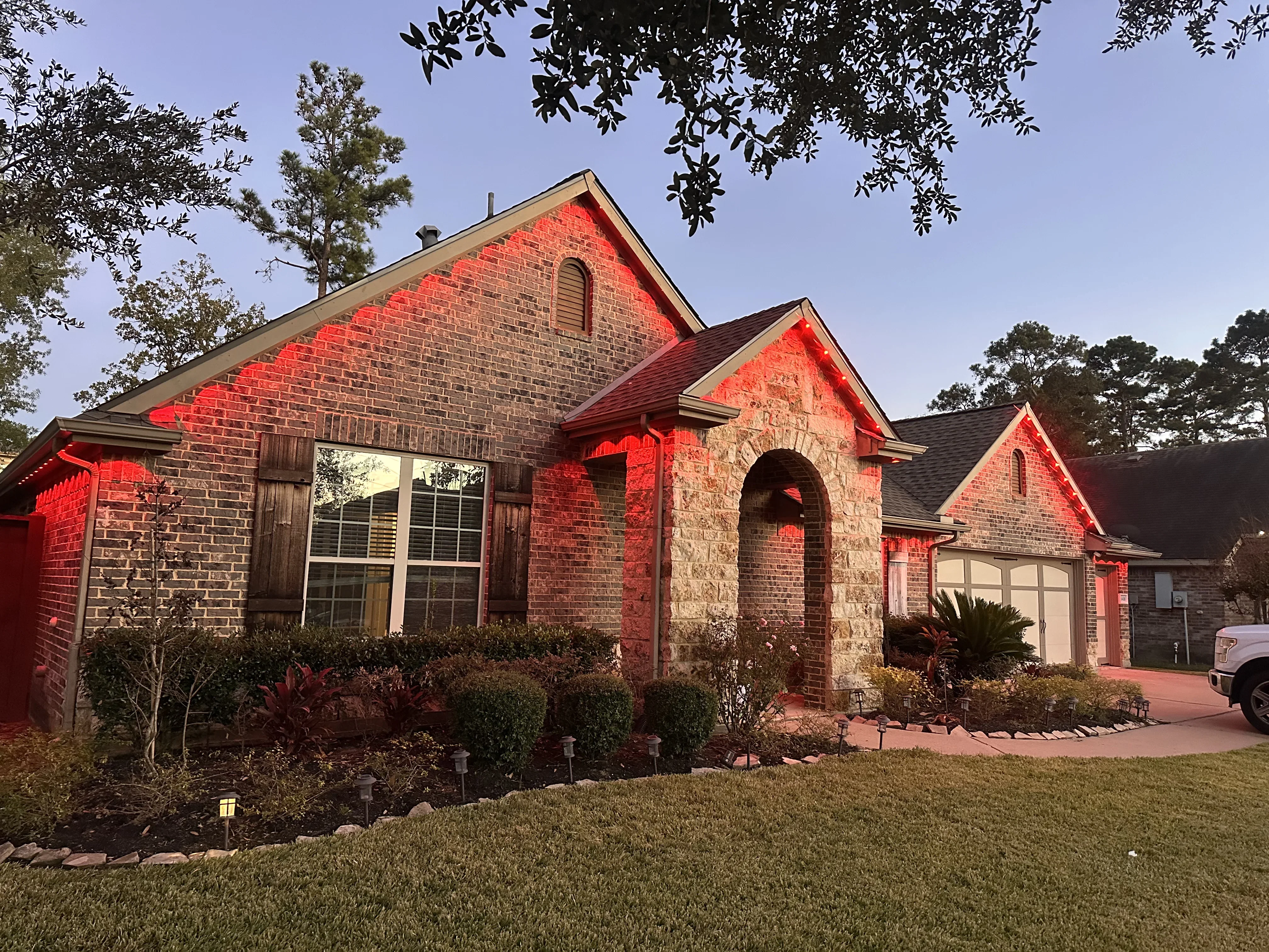 Red accent lighting on brick and stone home facade with uplighting on gables and arched entry