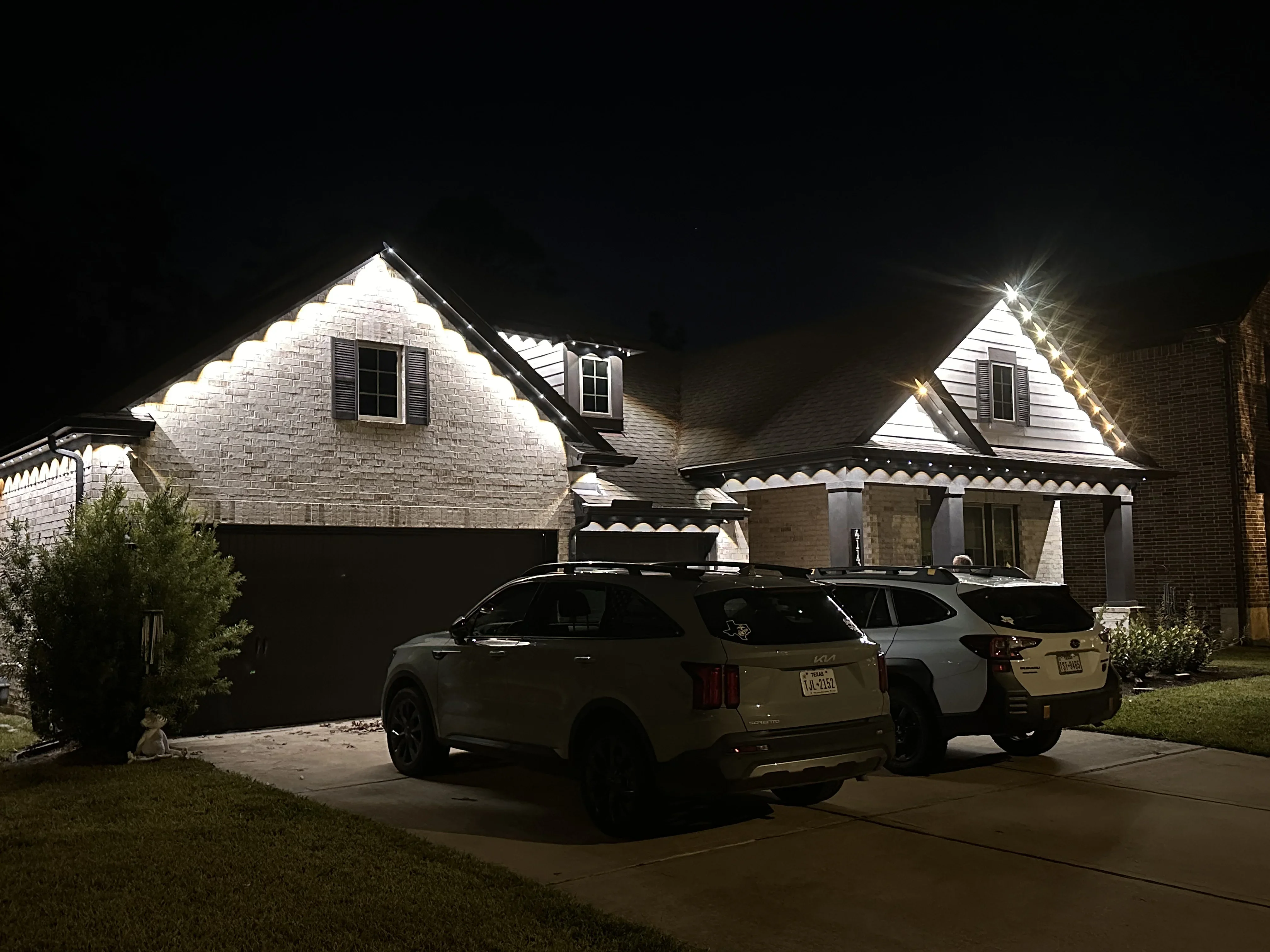 Brick home with white uplighting on gables and roofline at night