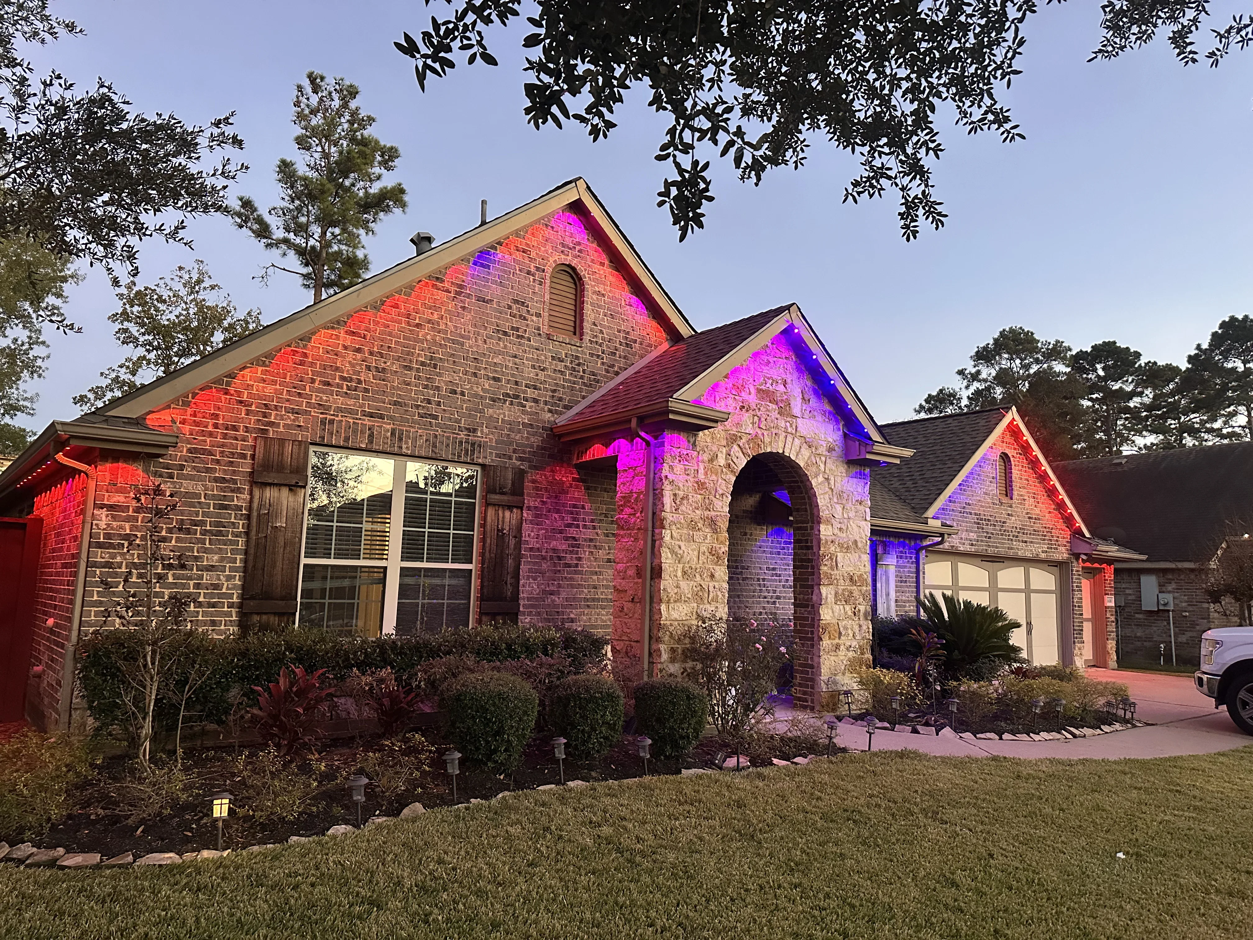 Brick and stone home facade with red and magenta RGB accent lighting on gables and arches