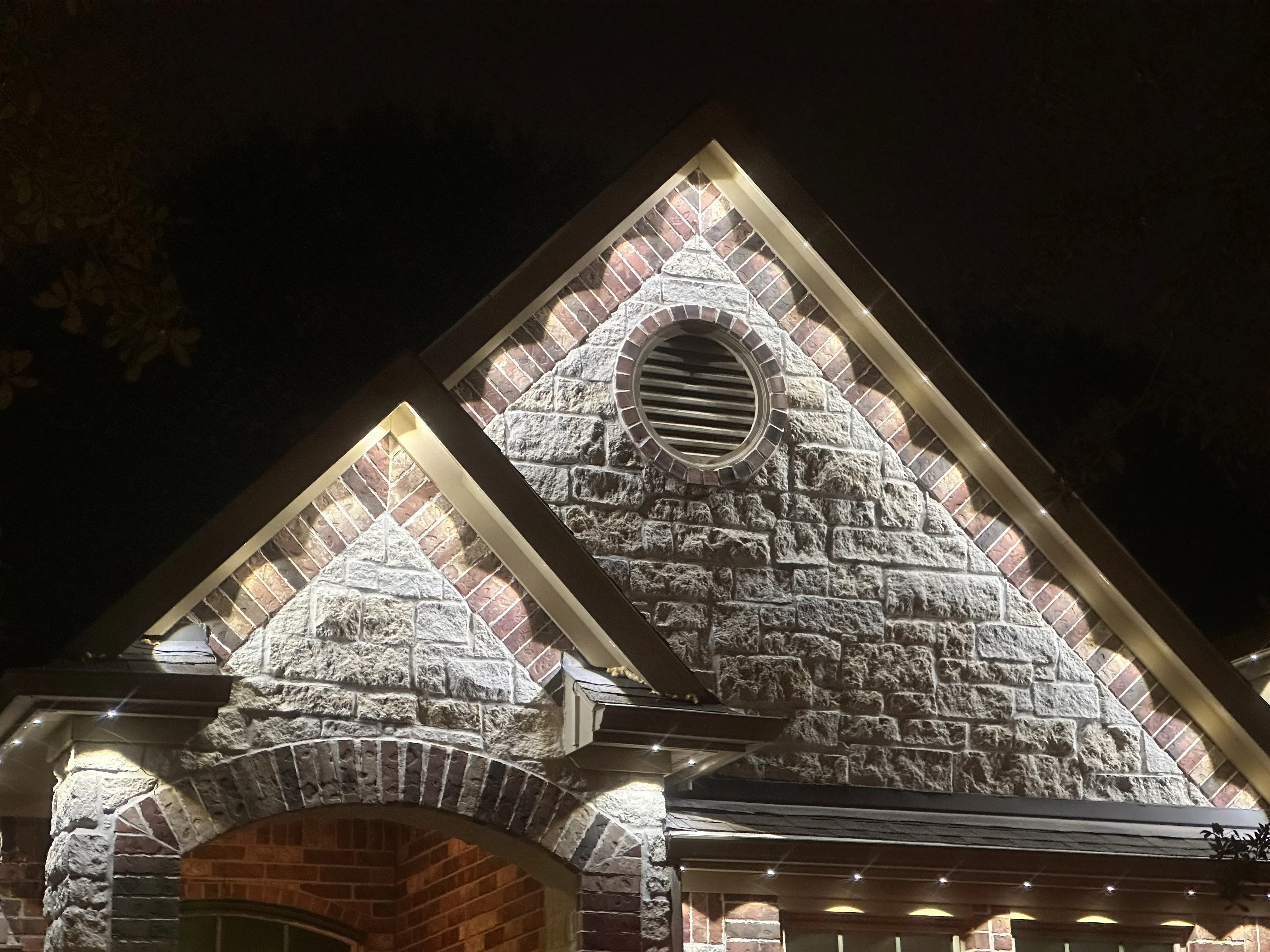 Stone gable peaks with LED uplighting illuminating textured masonry and brick architectural details at night