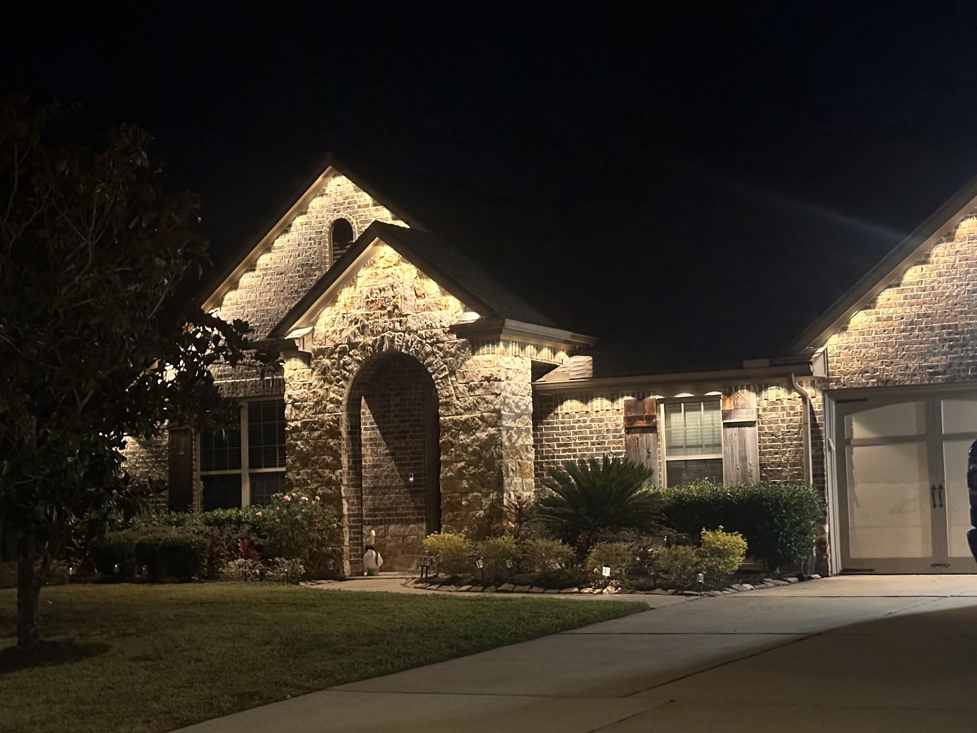 Brick home exterior with warm accent lighting on facade and landscape features at night