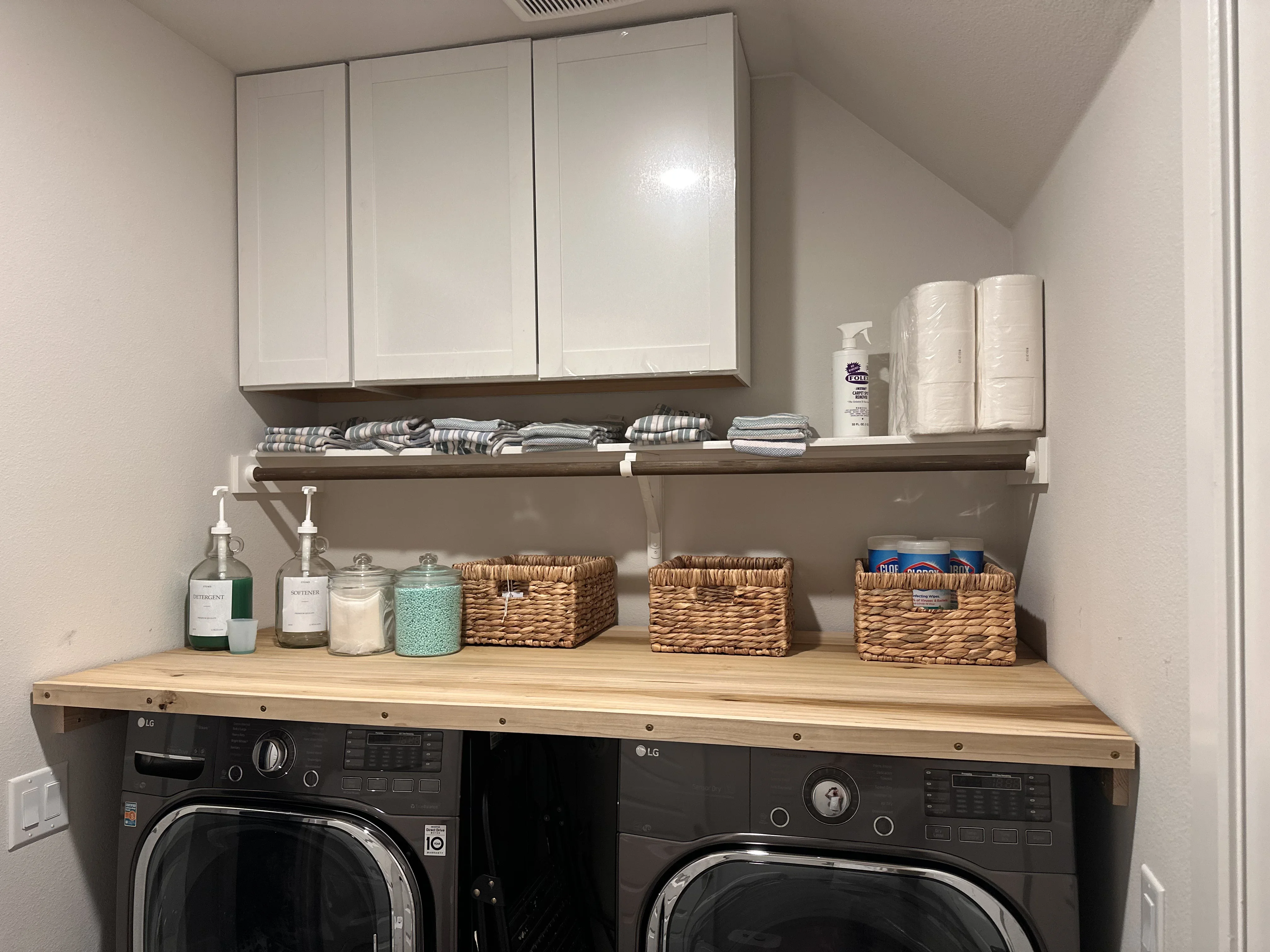 White cabinetry and wood shelving above black LG washer and dryer with woven storage baskets