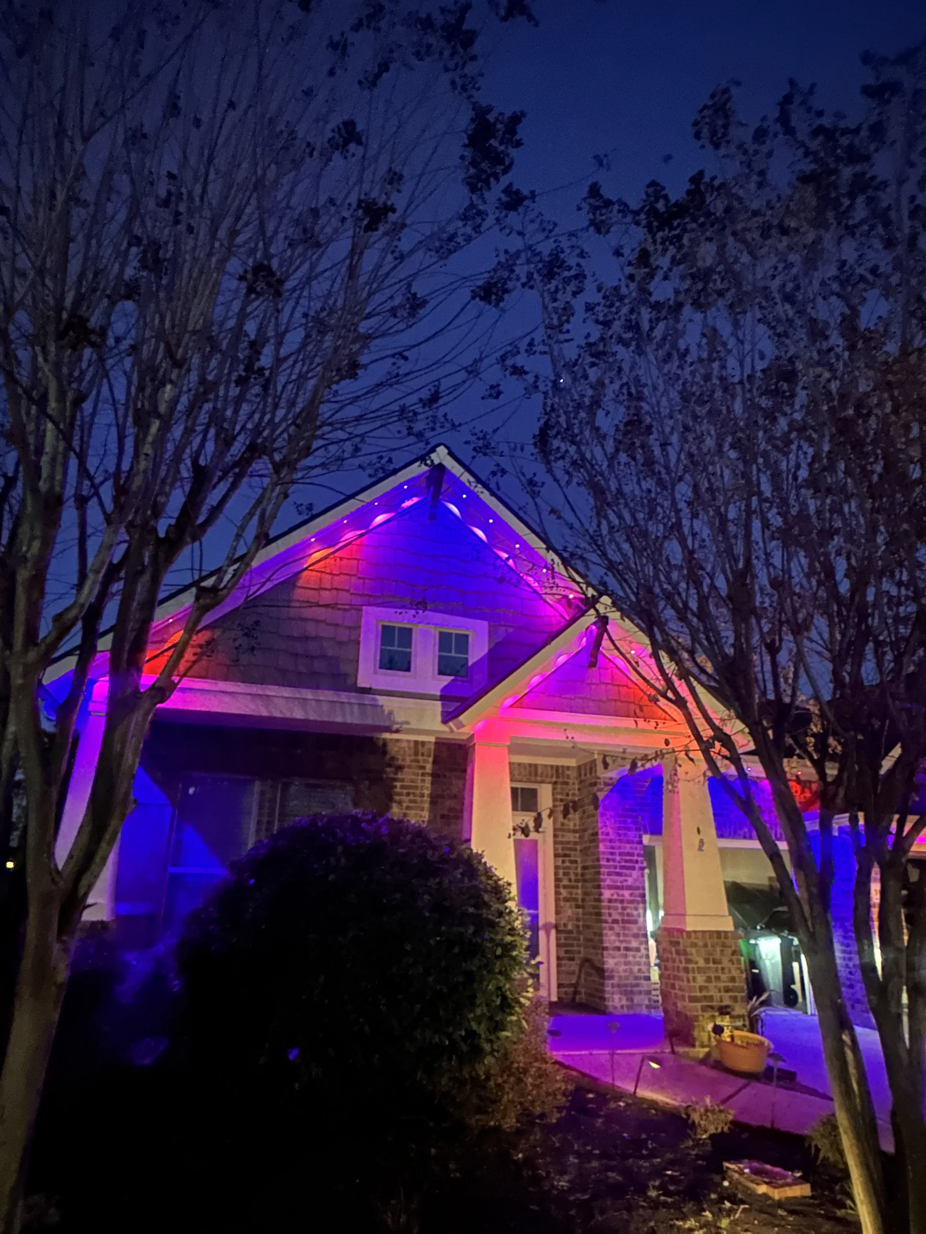 Brick home with purple and pink RGB LED accent lighting on roofline, gable, and front facade at dusk