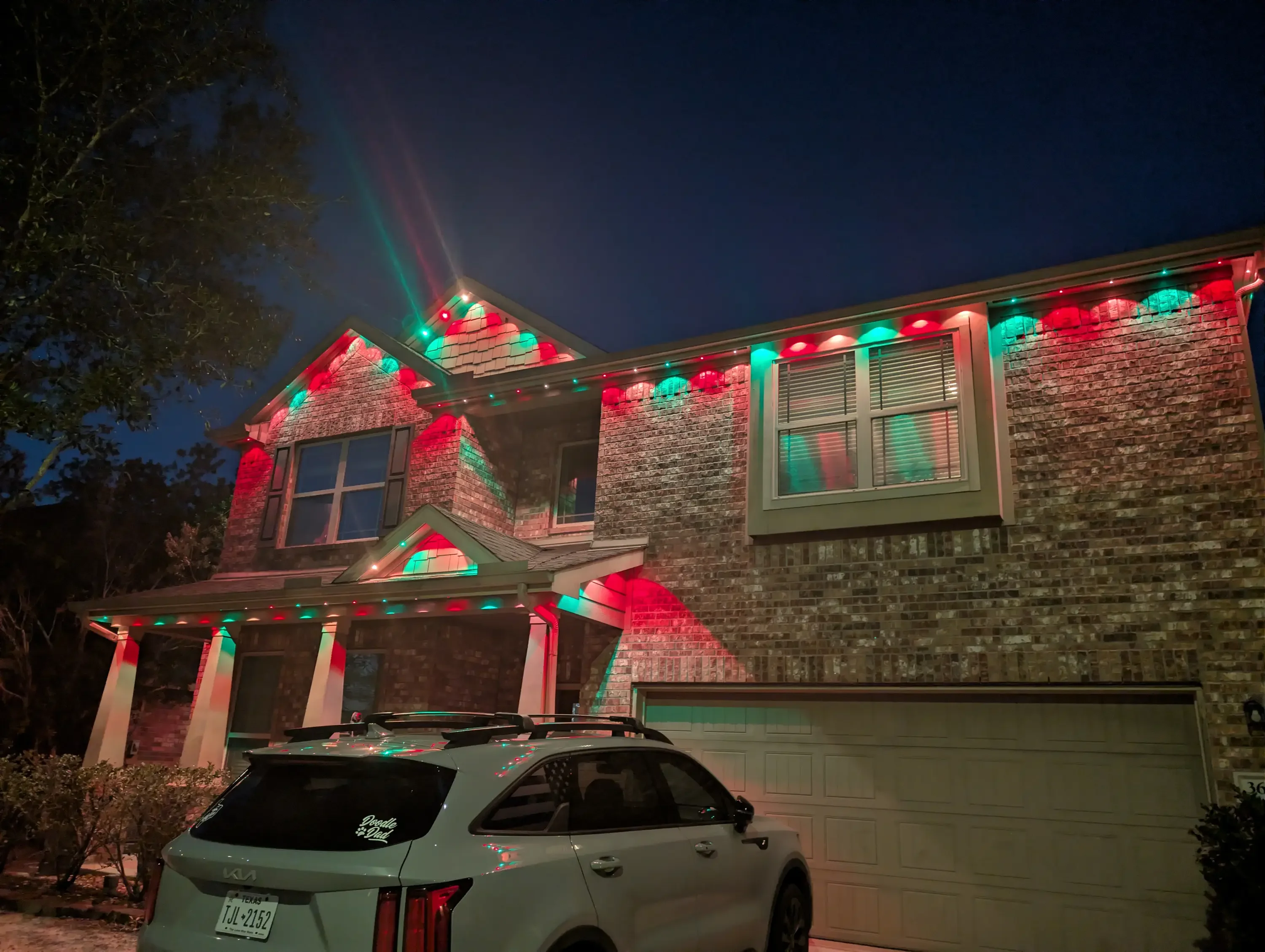 Two-story brick home at night with red and green LED roofline and gable lighting