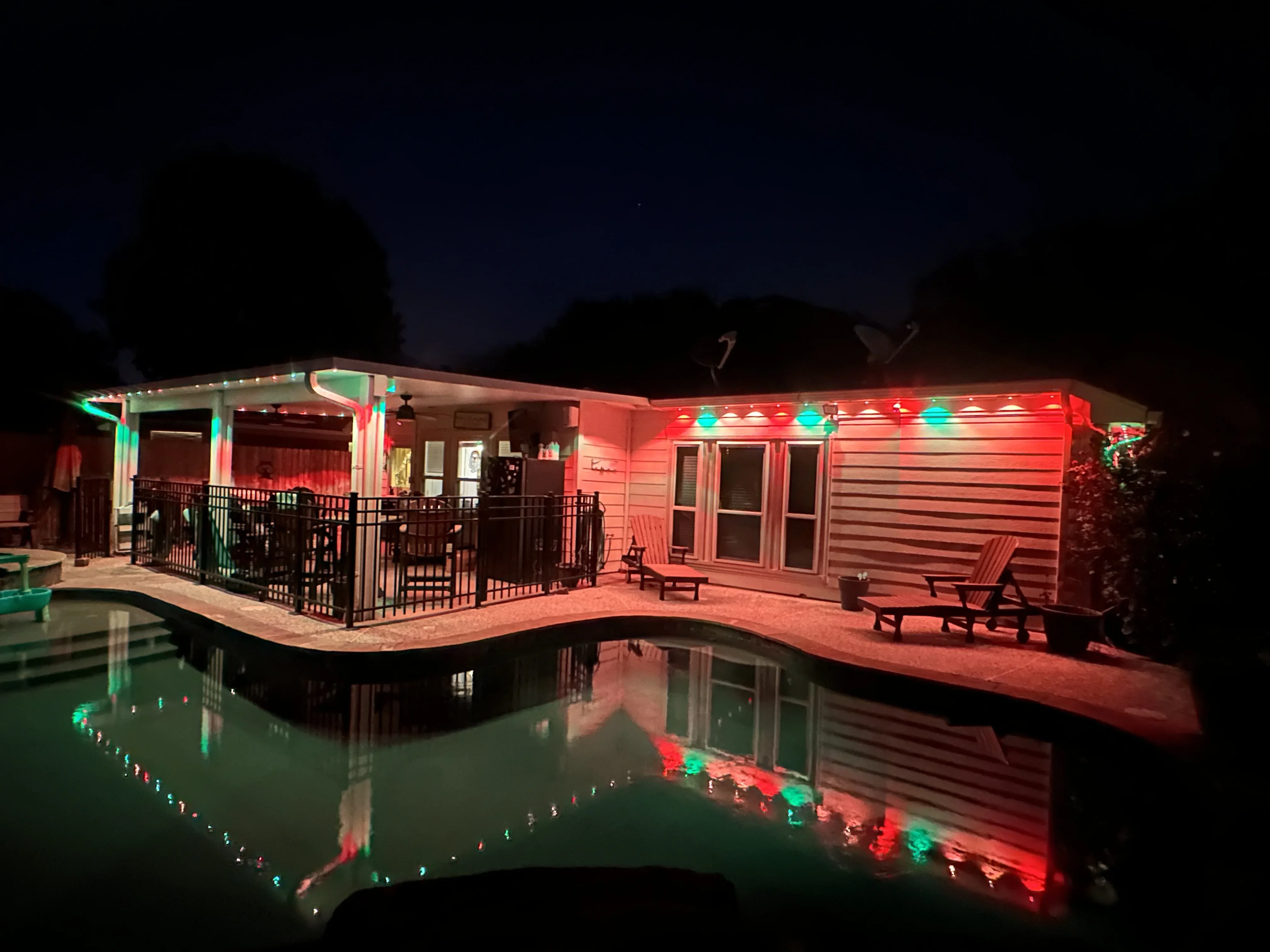 Red and green LED lights installed on house exterior, patio, and pool edge at night