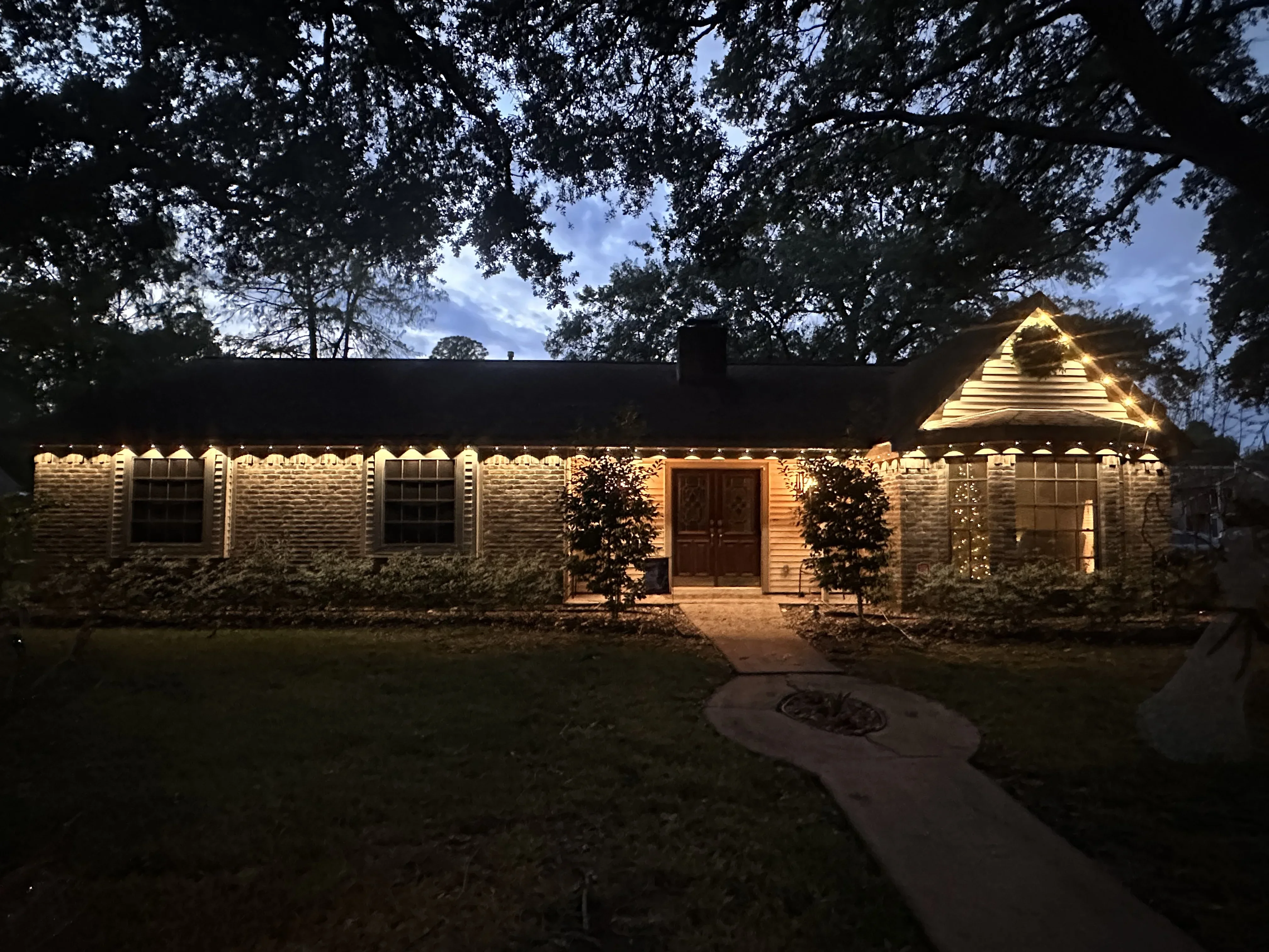 Stone residential building with warm uplighting on facade, gable roof, and entrance doors at dusk