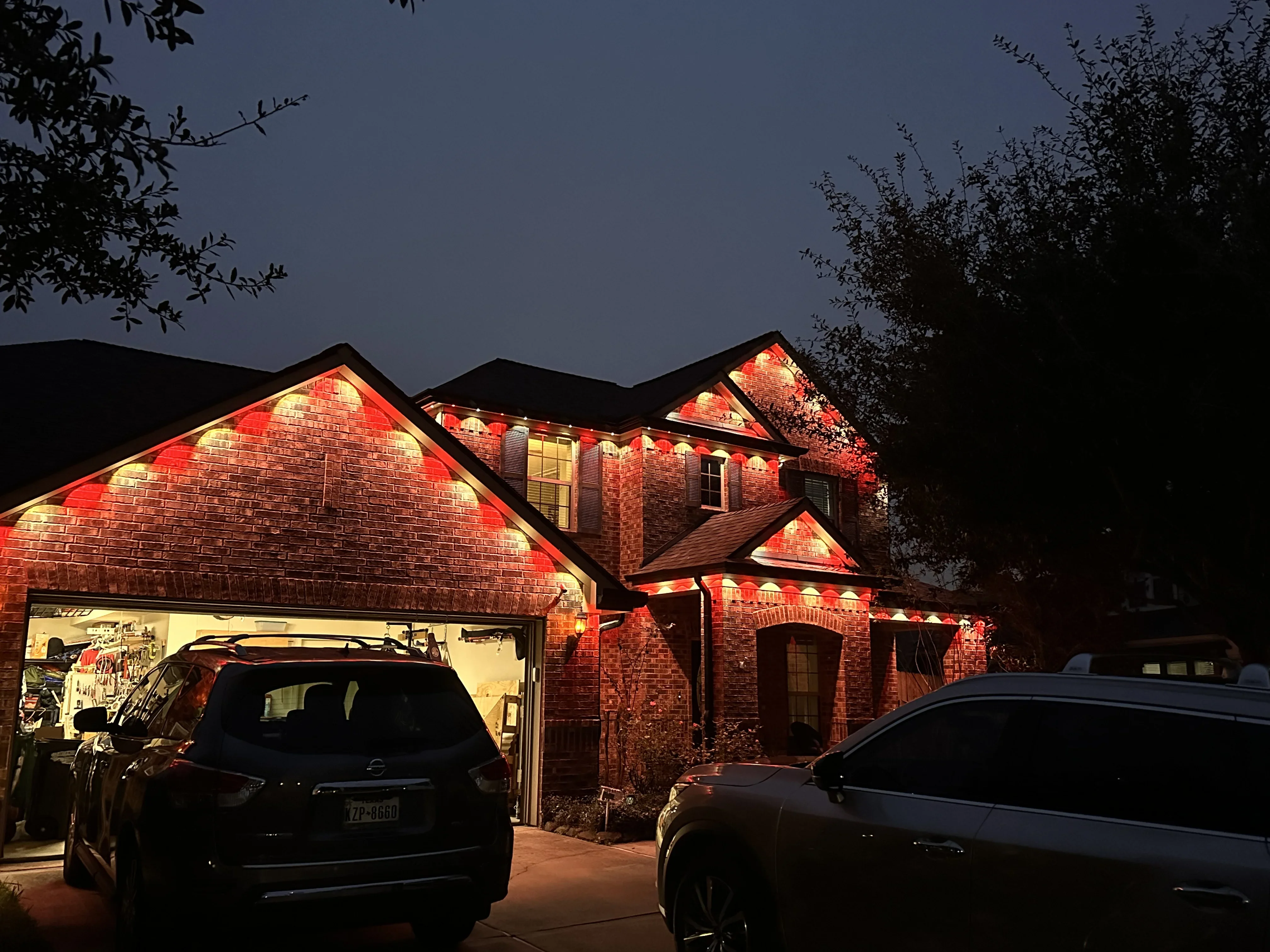 Brick home exterior with warm accent lighting on facade, gables, and architectural features at dusk