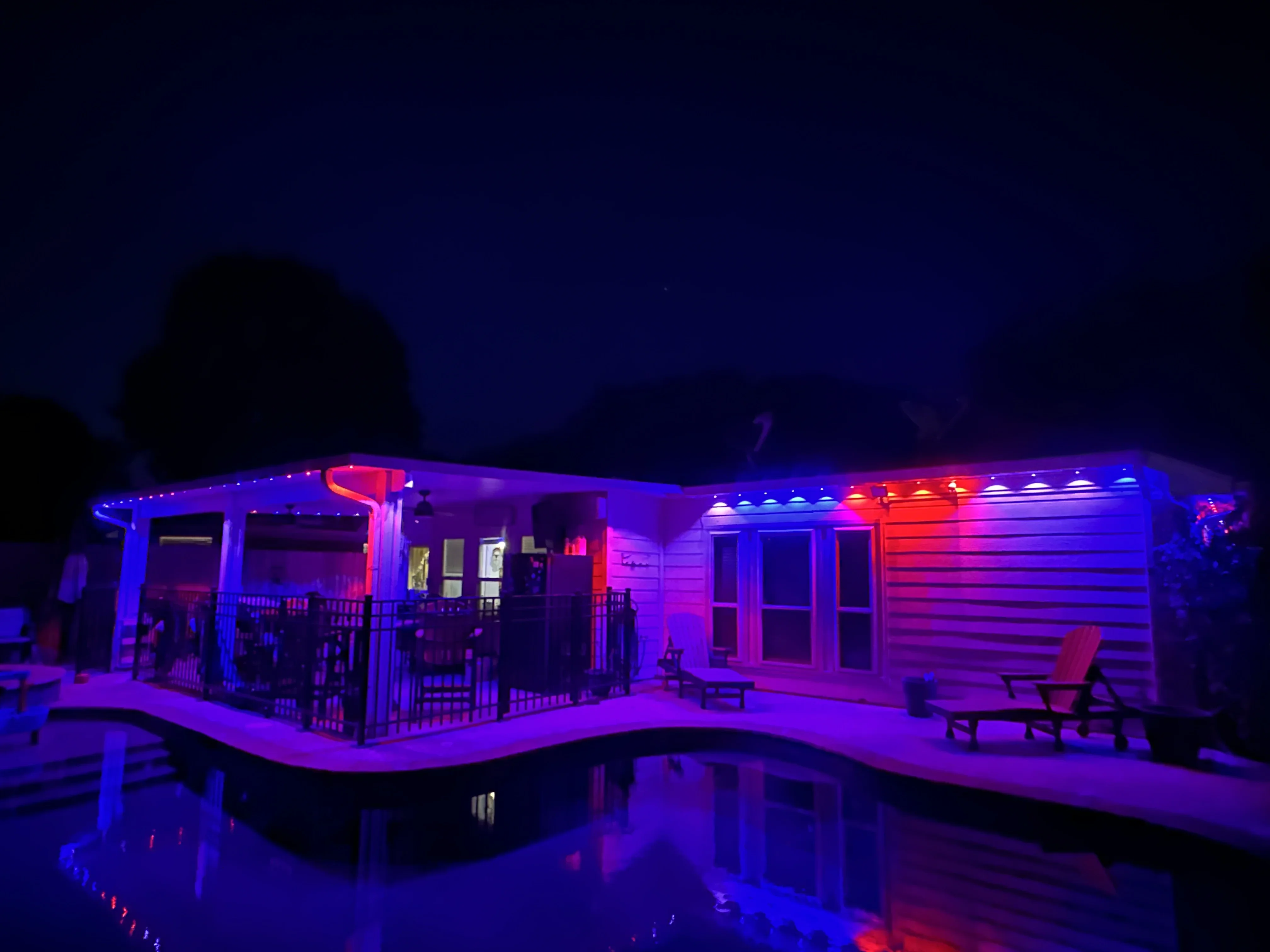 Modern home at night with blue and magenta RGB LED lighting on exterior, deck, and garage