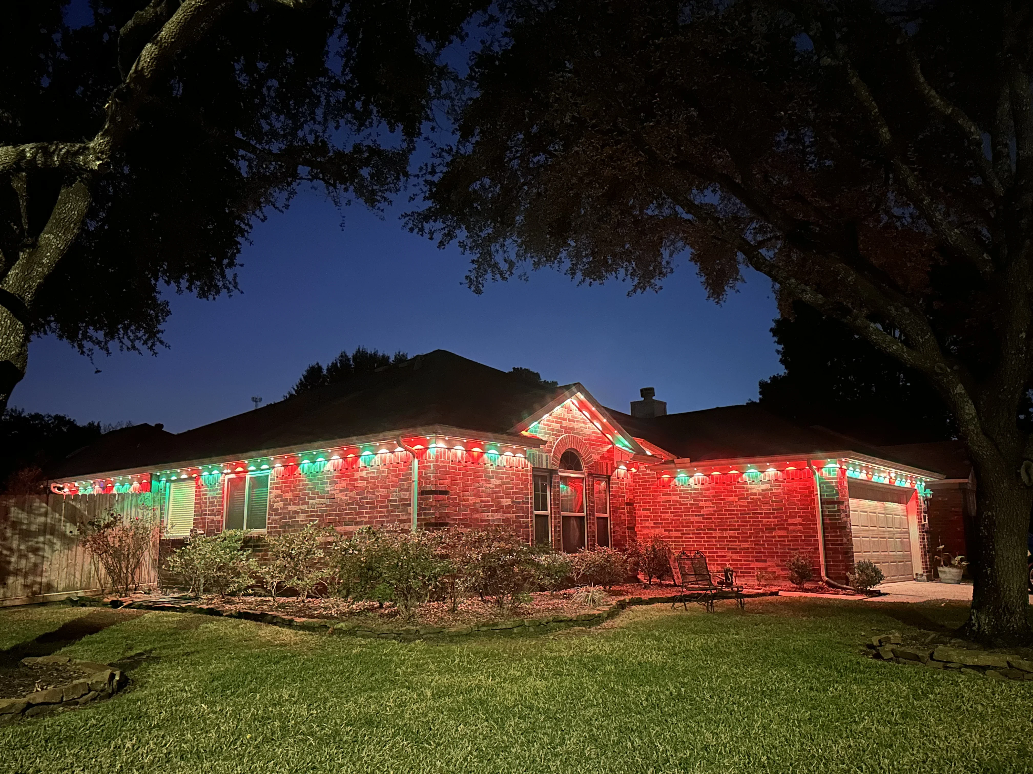 Red and green LED lights installed along roofline and soffit of brick home at dusk