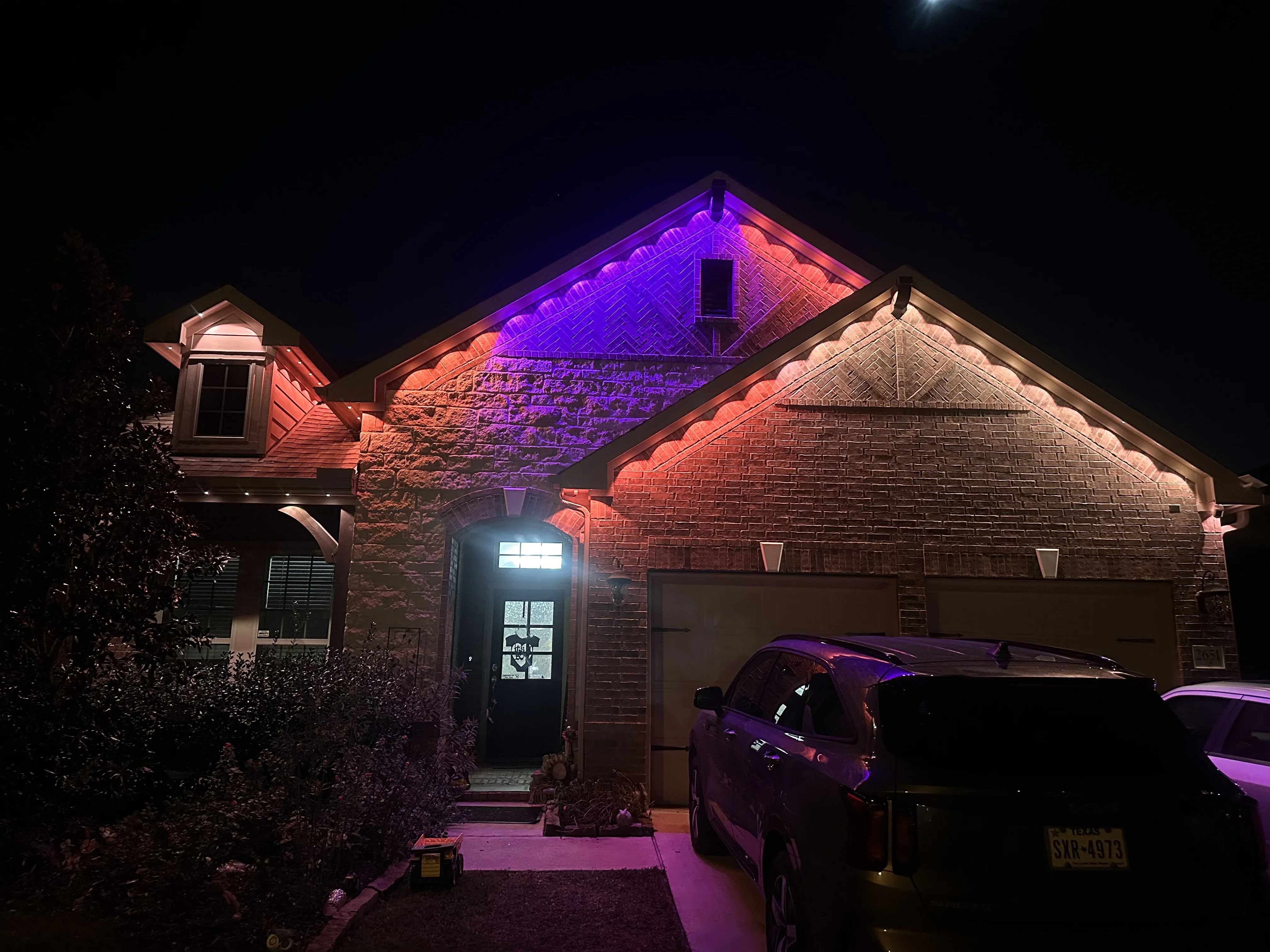 Brick home with purple and orange LED accent lighting on roofline and gable at night