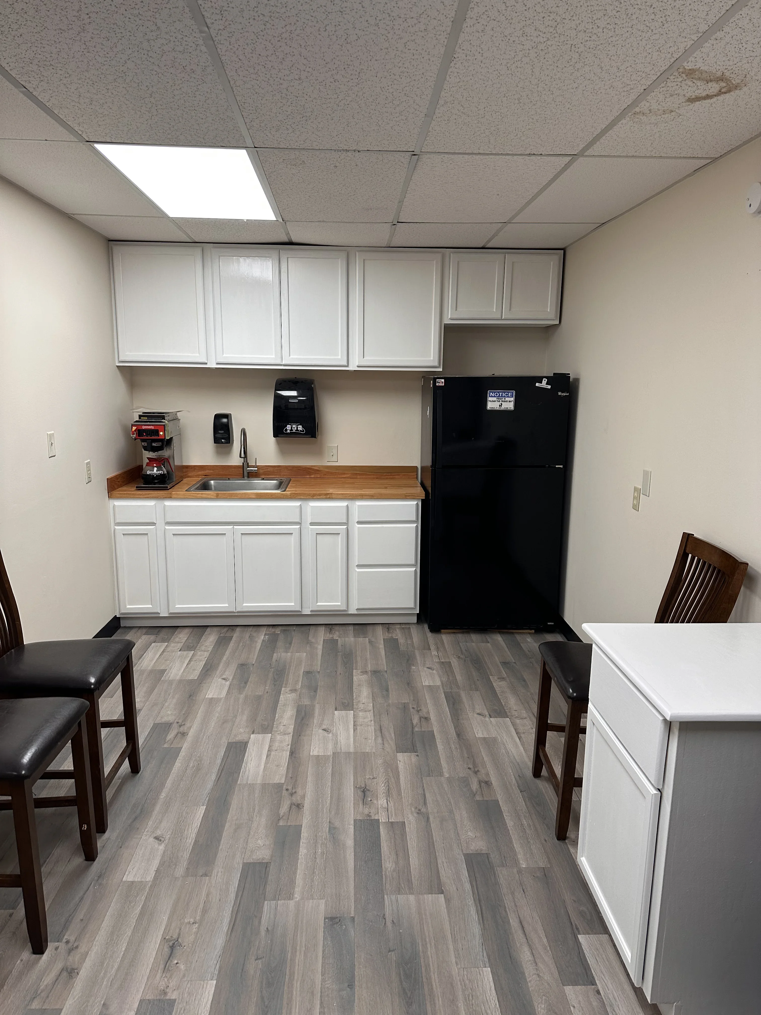 Recessed ceiling lights in drop-tile ceiling above white cabinetry with wood countertop and electrical outlets