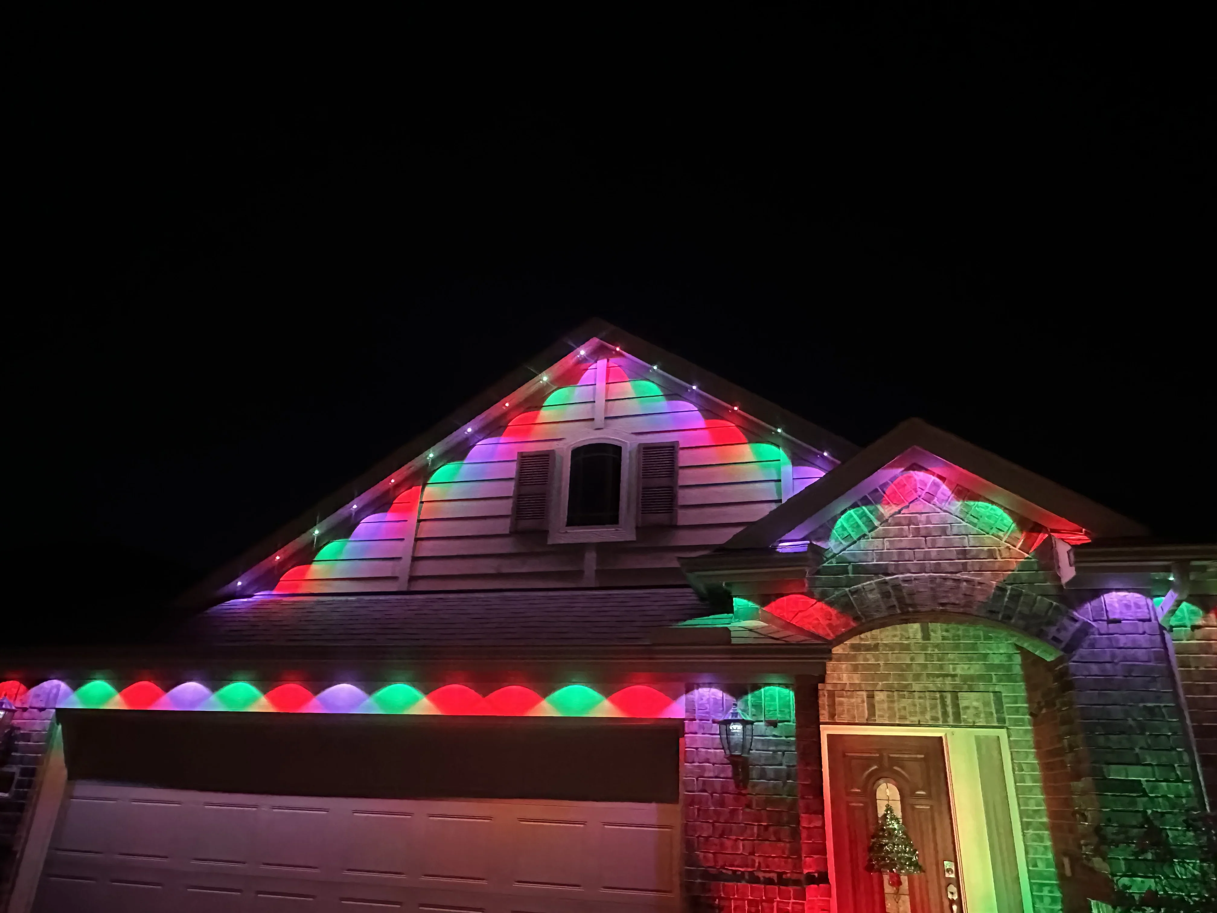 Brick home with RGB LED lights illuminating gable, soffit, and architectural features in multicolor patterns