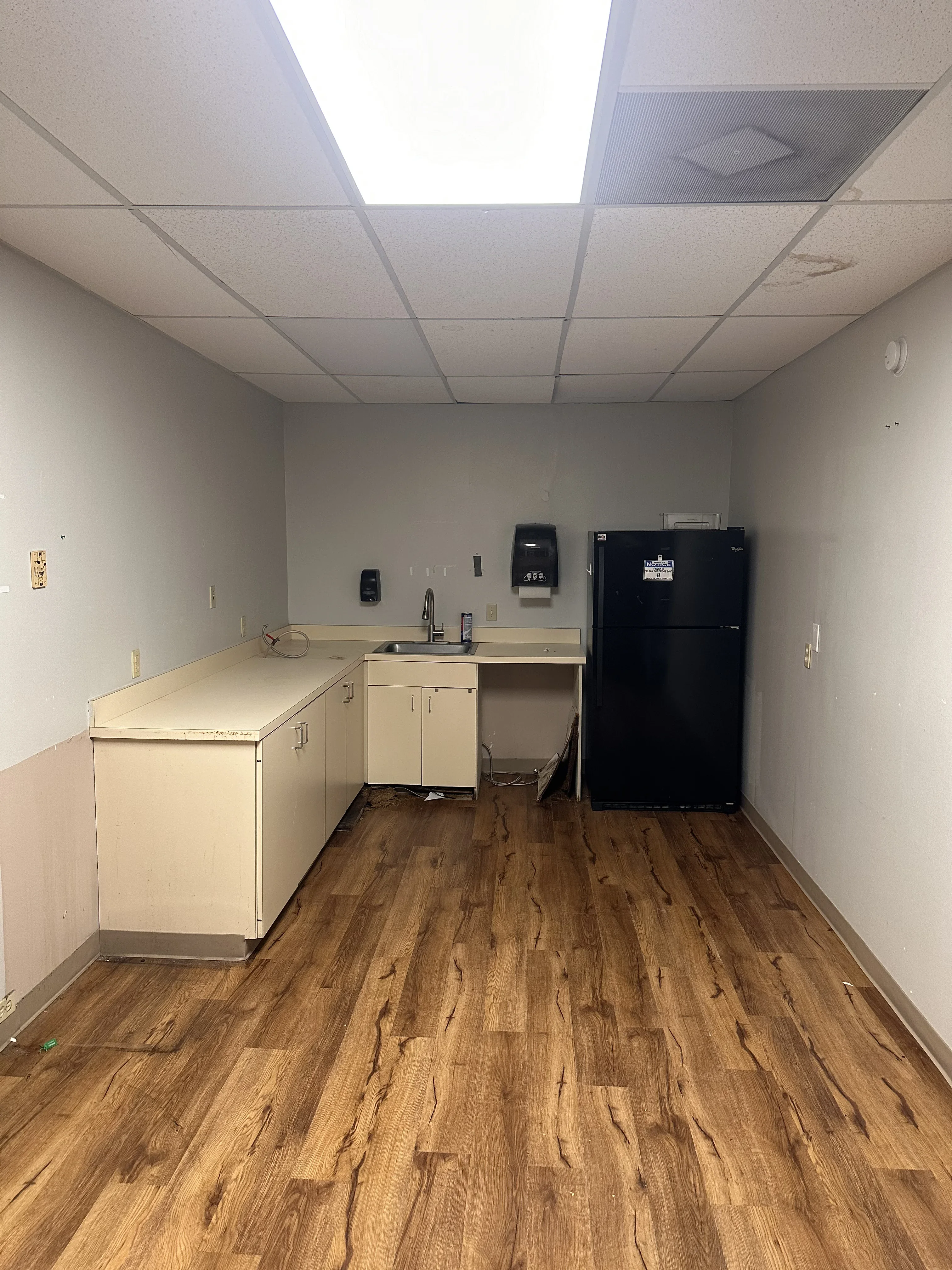 Recessed LED panel ceiling lights with drop ceiling grid in commercial break room with wood flooring