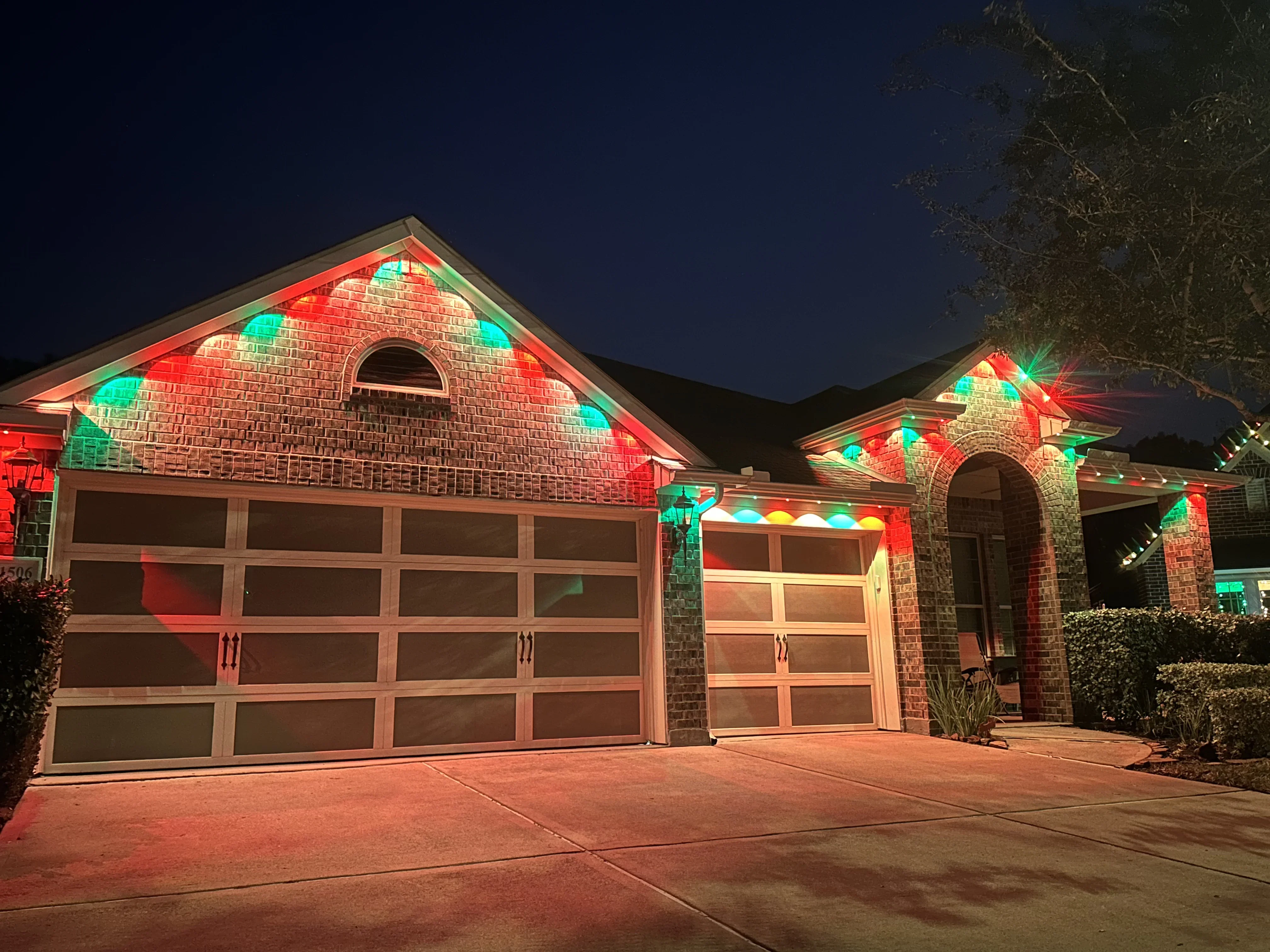 Brick home facade with red and green LED uplighting on gables, garage doors, and stone columns at night
