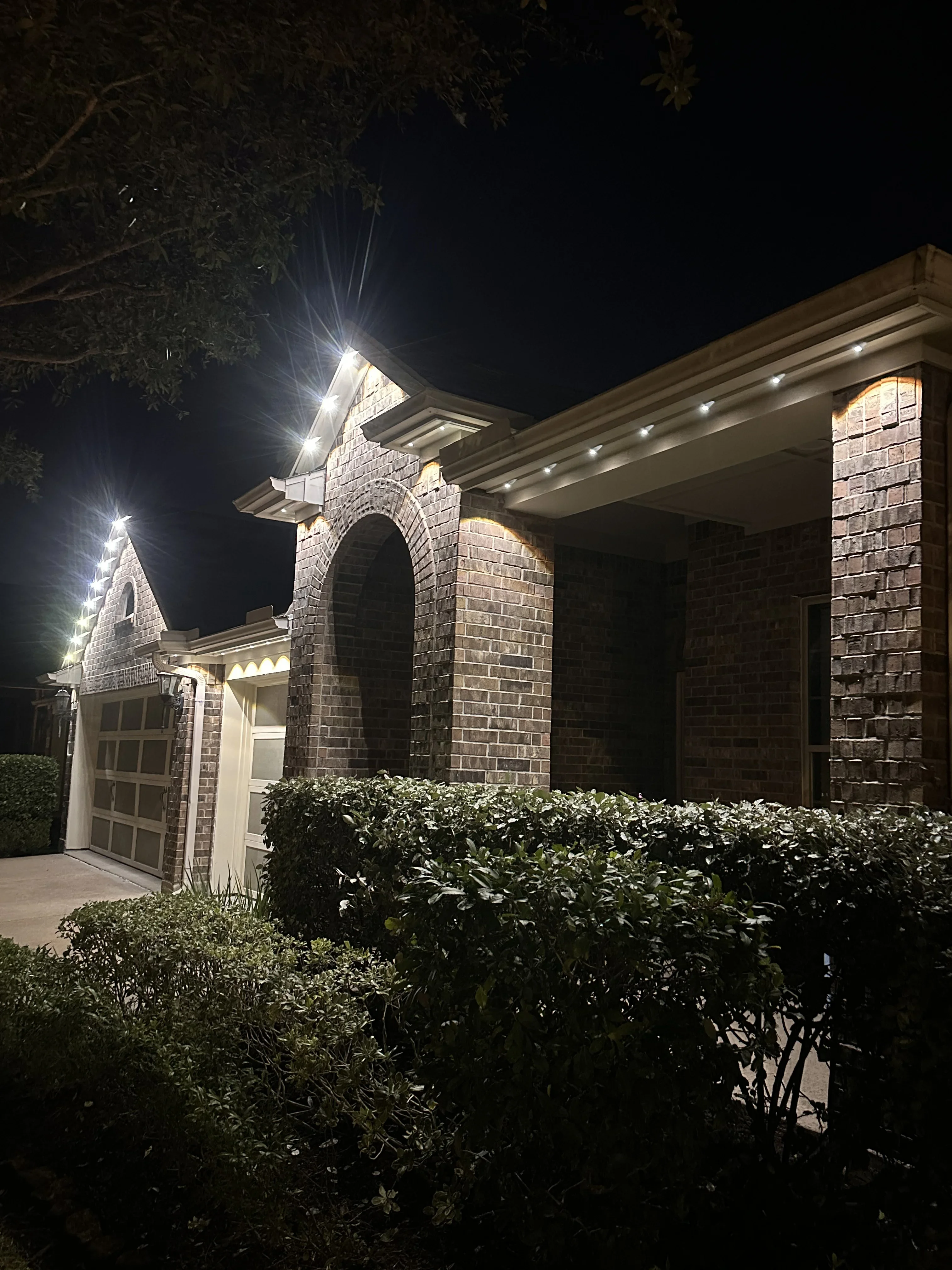 Brick home exterior with recessed soffit lights, archway accent lighting, and facade uplighting at night