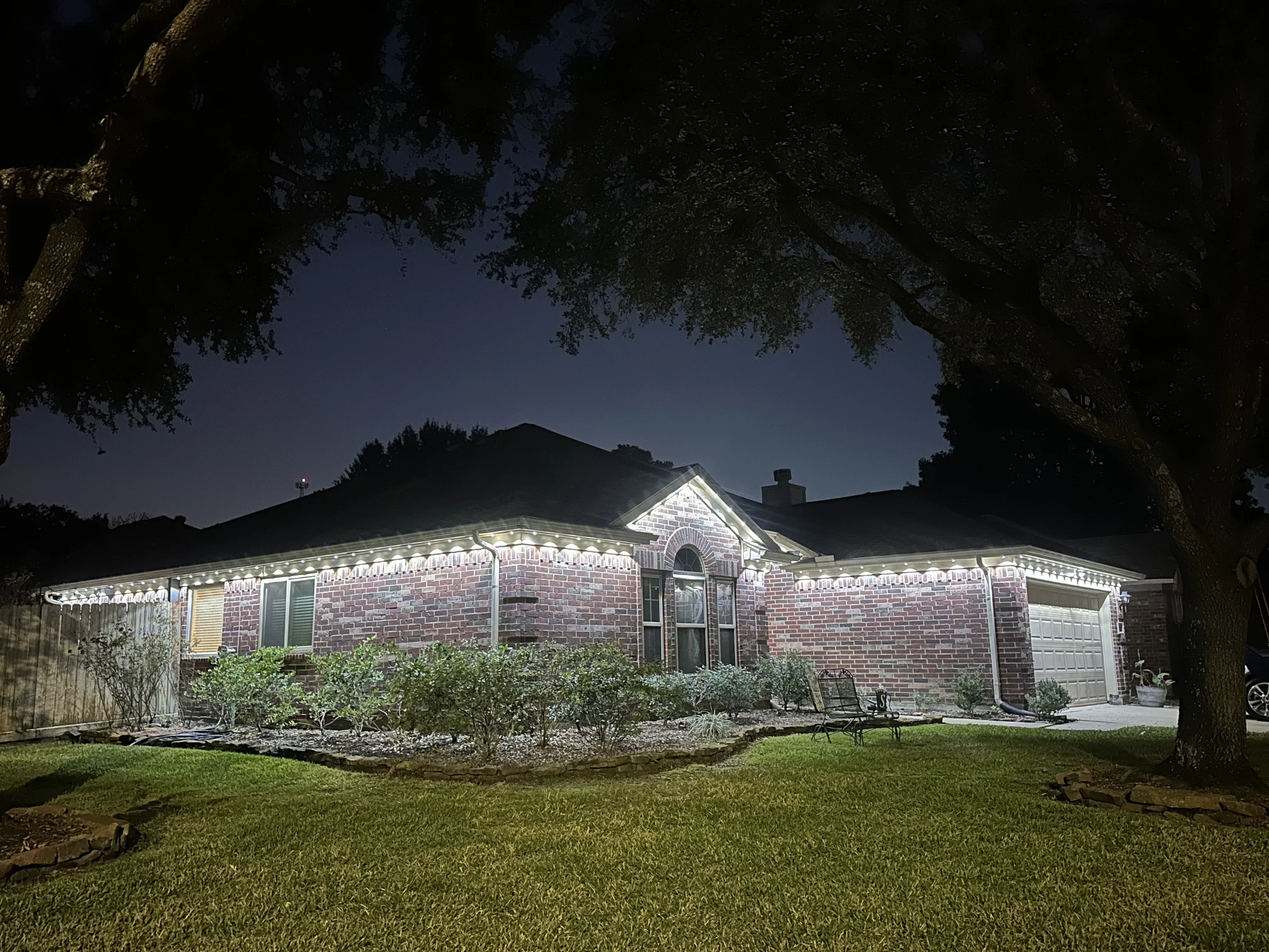 Brick home at night with professional exterior lighting highlighting roofline and landscaping